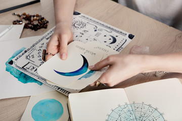 cropped view of astrologer holding cards with watercolor drawings by birth chart with zodiac sign on