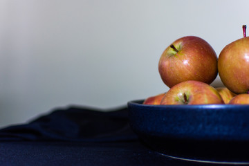 Apples in ceramic plate on the table covered black cloth