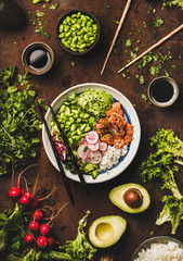 Healthy lunch, dinner. Flat-lay of salmon poke bowl or sushi bowl with various vegetables, greens, sushi rice, soy sauce over rusty table background, top view. Traditional Hawaiian, clean eating food