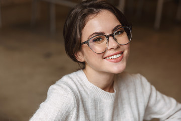 Canvas Print - Image of young woman wearing eyeglasses smiling at camera indoors