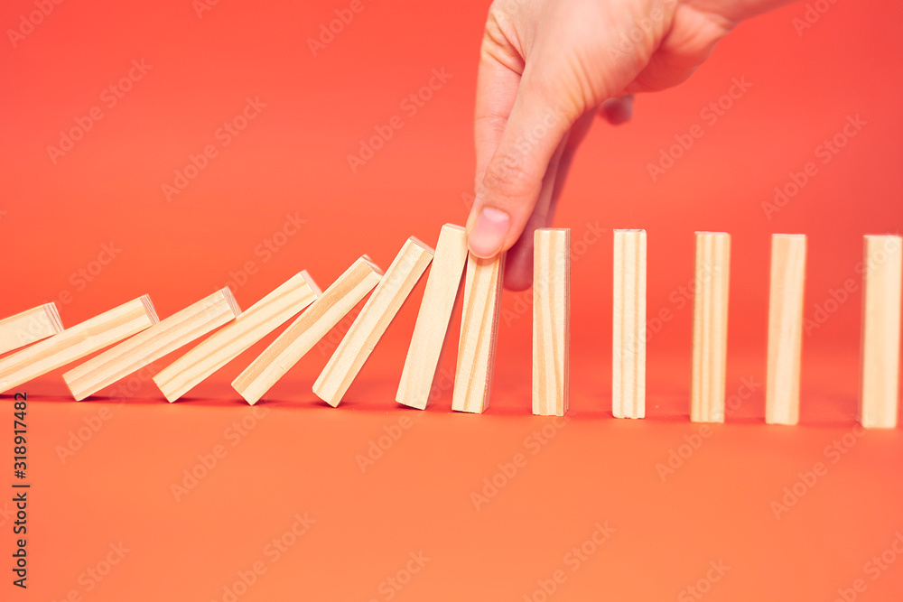 hand finger stops falling wooden dominoes, red background, domino principle, business concept - obrazy, fototapety, plakaty 