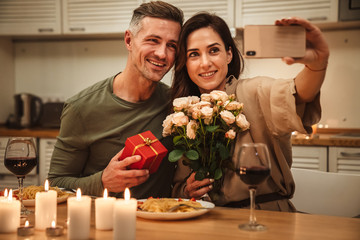 Wall Mural - Image of couple taking selfie while having candlelight dinner at home