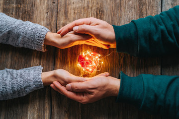 Wall Mural - Two hands holding a red heart shape covered with led lights on wooden and bokeh lights background. Valentines day and romance concept.