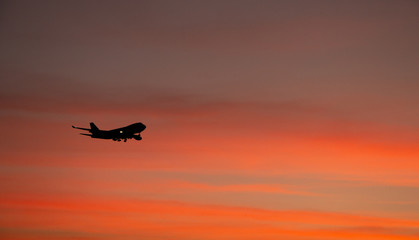 Silhouette of big airplane on beautiful orange sunset background, fast aerial transport, traveling and voyage concept