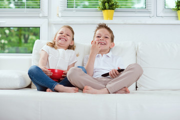 Little brother and sister watching tv on couch