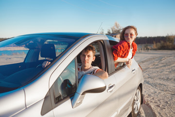 Pretty young couple driving the car at sea shore. Woman and man having fun at the trip. People traveling on automobile.