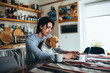 © cherryandbees - young man holding his dog in nap while using laptop in kitchen
