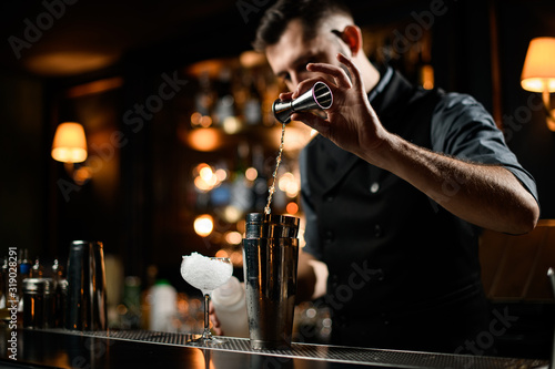 Fotografía Male bartender flows alcohol from small jigger to shaker