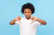 Dislike! Portrait of dissatisfied upset little boy with curly hair showing thumbs down gesture and looking displeased, naughty child making disagree disapprove finger sign. studio shot blue background