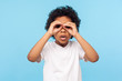 © khosrork - Curious child exploring world. Portrait of inquisitive nosy little curly boy looking through fingers shaped like binoculars and expressing amazement. indoor studio shot isolated on blue background