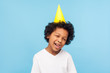 Portrait of humorous funny naughty little boy with party cone on head sticking out tongue and winking at camera, carefree child teasing, showing goofy foolish grimace. studio shot, blue background