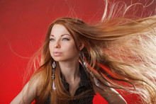 Beautiful Girl With Hair Flying In The Wind. Model With Long Hair. Woman With Voluminous Hairstyle. Beauty Lady On A Red Background.