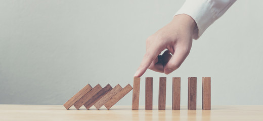 hand stopping wooden domino business crisis effect or risk protection concept