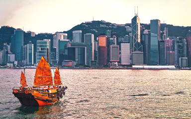 Wall Mural - Junk boat at Victoria Harbor of Hong Kong at sunset. View from Kowloon on HK Island.