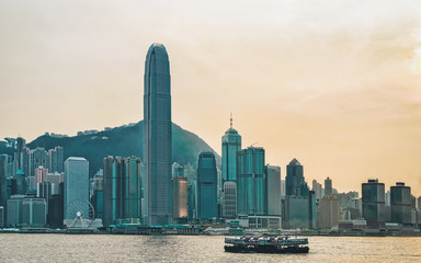 Wall Mural - Star ferry in Victoria Harbor and HK skyline at sunset. View from Kowloon on Hong Kong Island.