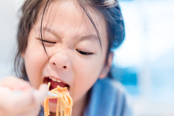 Wall Mural - Hungry face and enjoy eating concept.Little asian girl enjoy eating with spaghetti bolognese with cheese on a plate in lunch time at restaurant.