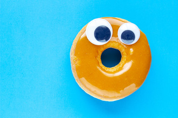 a canadian maple dip donut with black wiggle googly eyeballs on a blue background
