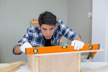 Young asian carpenter working on wooden job with spirit level - Handyman and diy concept