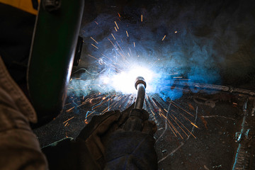 Man with mask welding steel between smoke and sparks