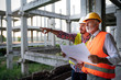 © NDABCREATIVITY - Two satisfied engineers talking at building site with construction structure in background