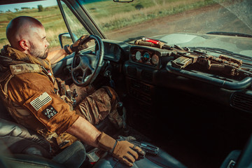 Bald soldier in uniform is driving military vehicle.