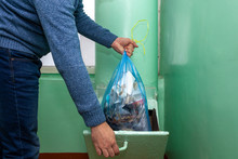 Throwing Garbage In Refuse Chute In Russia. A Man Throws Out Garbage In A Blue Plastic Bag . Old Multi-storey Building.