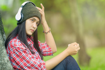 asian women wearing a hat, listening to music with white headphones, holding a cup of coffee on a weekend morning