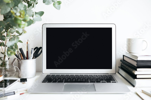 Modern cozy workplace of student with laptop computer with copy space display, textbooks and stationary accessories on white desk. Interiors, design, style, technology and education concept