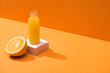 fresh juice in glass bottle near orange half and white cube on orange background