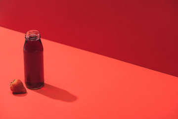 fresh berry juice in glass bottle near ripe strawberry on red background