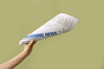 Female hand with newspaper rolled as megaphone on color background