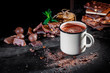 Portion of homemade mint hot chocolate in a cup with chocolate and nuts on dark background