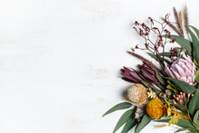 Beautiful Flat Lay Floral Arrangement Of Mostly Australian Native Flowers, Including Protea, Banksia, Kangaroo Paw Eucalyptus Leaves And Gum Nuts On A White Background. Space For Copy.