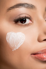 Wall Mural - close up of african american girl with heart of cream of cheek, isolated on pink
