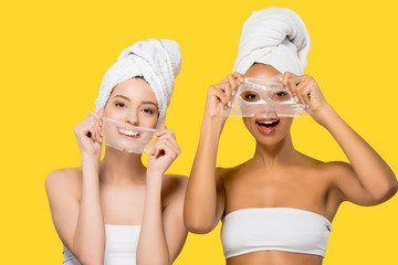 Wall Mural - happy attractive multiethnic girls holding hydrogel masks, isolated on yellow