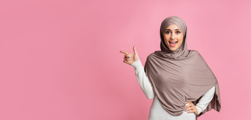 Happy islamic woman pointing aside at copy space on pink background
