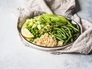 Wall Mural - Quinoa bowl with green beans, green peas, cucumber, avocado, and pine nuts on grey background. Copy space