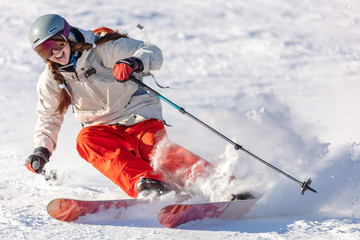 Girl On the Ski. a skier in a bright suit and outfit with long pigtails on her head rides on the track with swirls of fresh snow. Active winter holidays, skiing downhill in sunny day. Woman skier