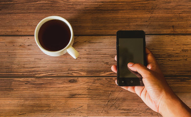 A mobile phone with a coffee cup on the wooden table