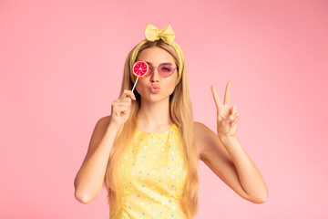 Excited girl holding lollypop over pink studio wall