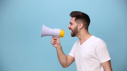 Wall Mural - Unshaven bearded young guy 20s wearing white t-shirt isolated on pastel blue background in studio. People sincere emotions lifestyle concept. Side scream in megaphone announces discounts sale Hurry up