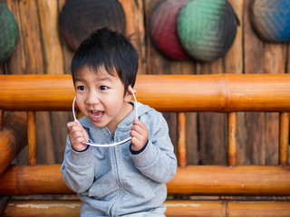 Asian funny child boy wearing sunglasses with happy laughing face outdoor in orange vintage wooden background. Fashion stylish.