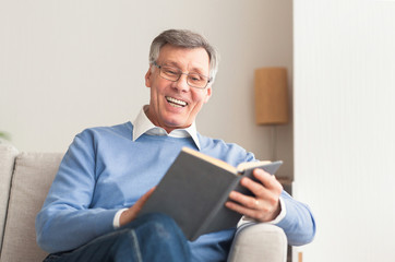 Wall Mural - Senior Man Reading Book Sitting On Sofa At Home