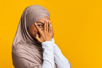 Wall Mural - Portrait of shy black muslim girl in headscarf peeking through fingers