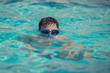 European boy in swimming goggles is swimming in the hotel’s pool during his summer vacations.
