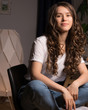 © Anna - Curly hair girl in casual clothes sitting on chair at home