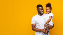 Happy African Man Holding Little Daughter Over Yellow Background