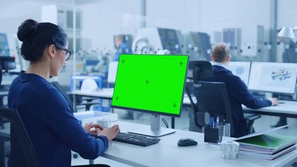 Fototapete - Over the Shoulder: Female Chief Engineer Working on Personal Computer, Display is Green Mock-up Screen or Chroma Key. Industrial Factory with High-Tech Machinery and Professional Workers