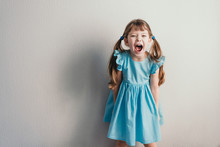 Screaming Little Girl In Blue Dress On Neutral Backgroung