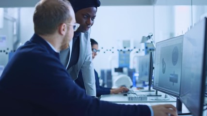 Modern Factory: Female Project Supervisor Talks to a Male Industrial Engineer who Works on Computer. They use CAD Software to Design Industrial Machinery in 3D. Working High-Tech Industrial Facility